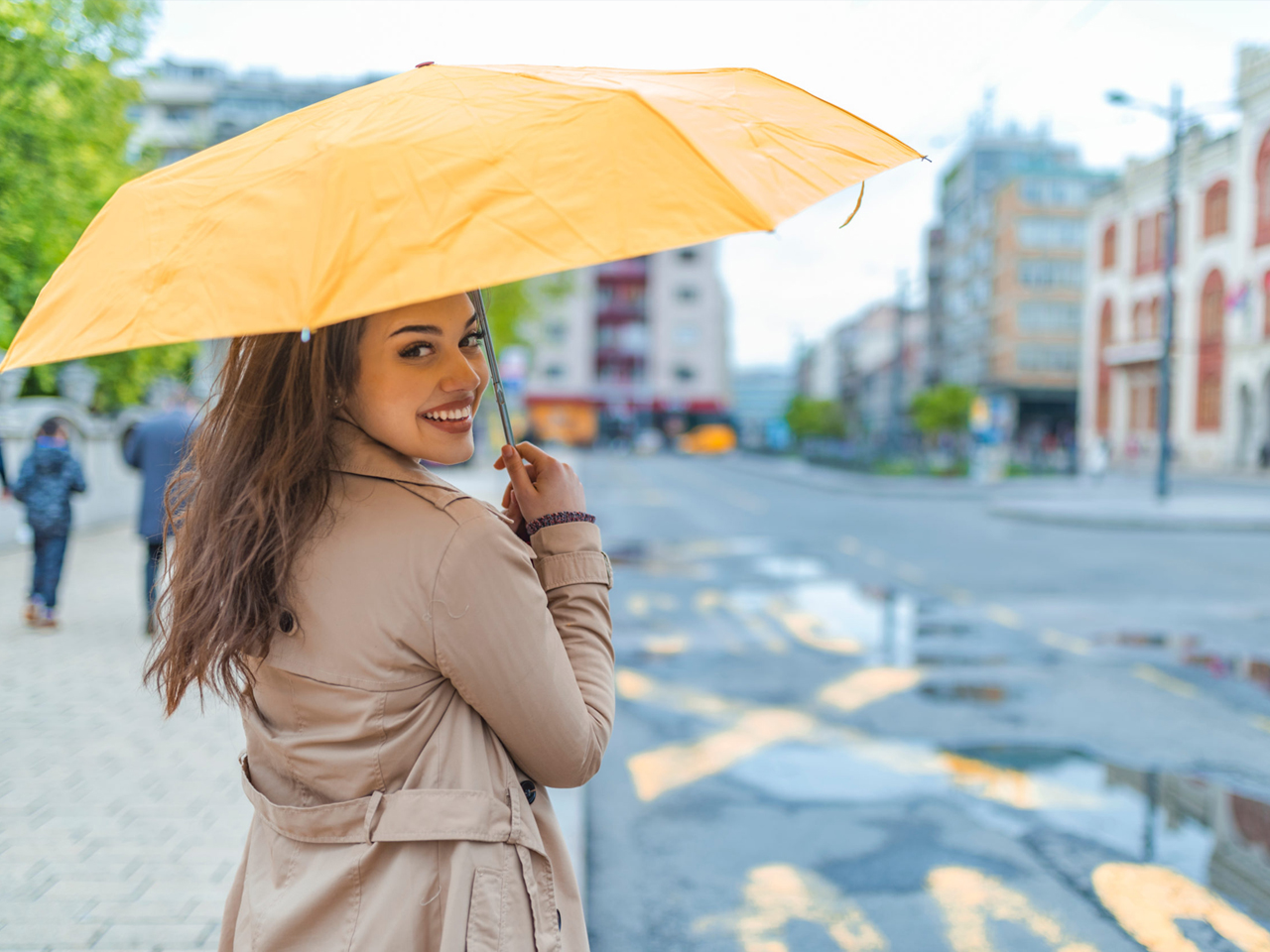 Smiling woman holding a yellow umbrella while standing on a city street during daylight - eastdouglasinsurance.com/
